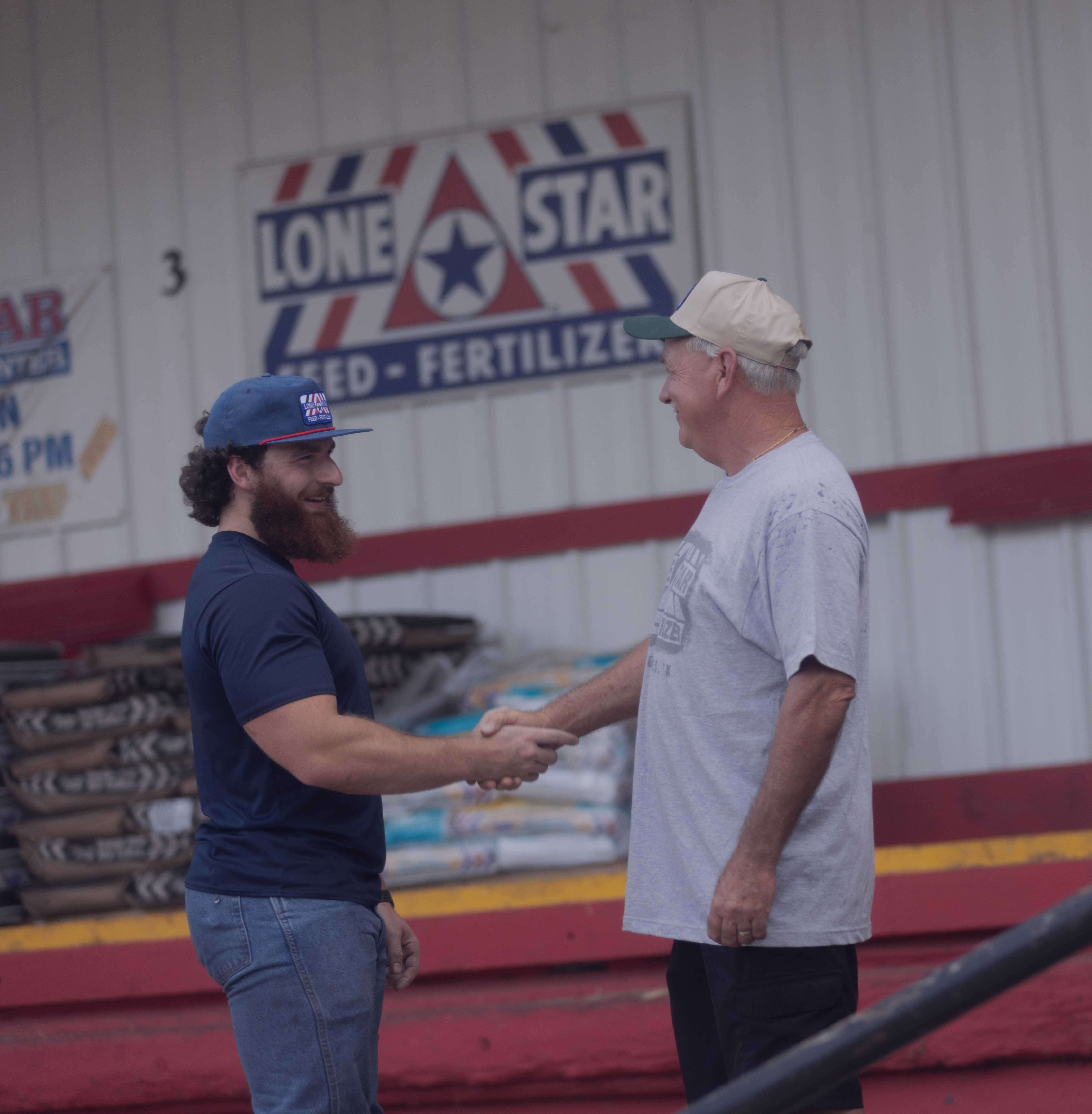 Two men smiling and shaking hands in front of a warehouse building.